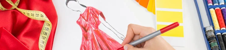 Hand sketching a red dress design next to fabric and color swatches with measuring tape and pencils.