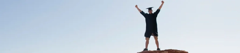 A graduate on the top of a mountain, arms outstretched in celebration: he's graduated from his HND