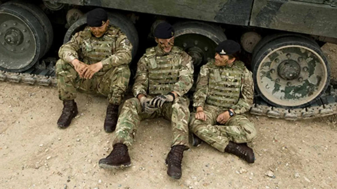 Three army officers resting against an armed vehicle