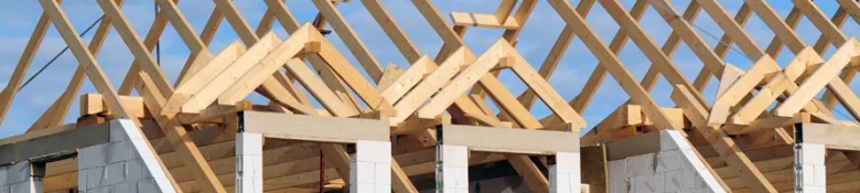 Wooden roof trusses on a partially constructed building against a clear sky.